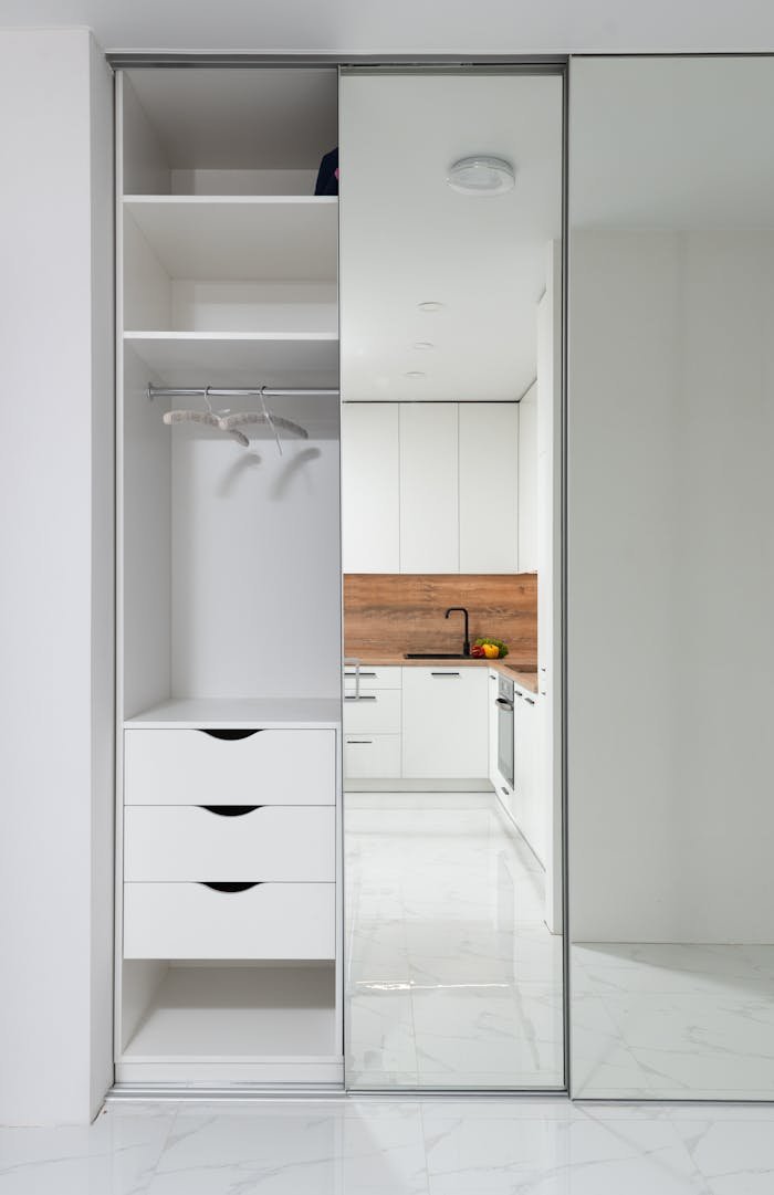 Wardrobe in hallway with mirrored wall reflecting furniture of modern kitchen in light apartment